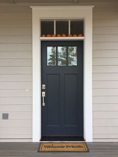 a blue front door with pumpkins on the top shelf and welcome mat in front