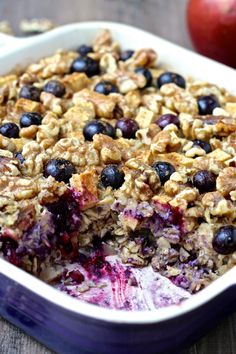 a blueberry baked oatmeal in a white dish next to an apple