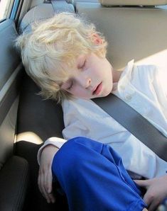 a young boy sleeping in the back seat of a car with his head resting on an arm rest