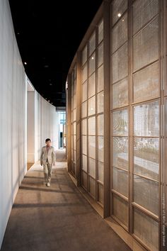 a man walking down a long hallway between two tall white walls with glass panels on each side