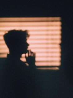 the shadow of a person holding a cell phone in front of a window with blinds