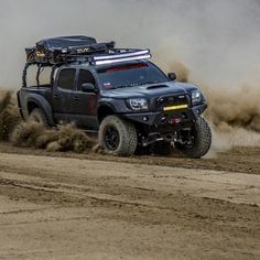 a black truck driving down a dirt road next to a hill covered in grass and bushes