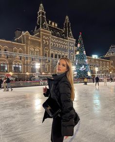 a woman is standing on an ice rink in front of a building with christmas lights