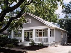 a small gray house with white trim and porches on the front, surrounded by trees