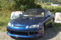 a blue sports car parked on gravel next to trees