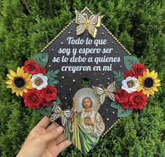 someone holding up a graduation cap decorated with flowers and an image of jesus on it