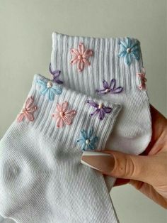 someone is holding two pairs of white socks with colorful flowers on the bottom and sides