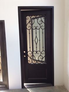 a black door with wrought iron bars on the top and bottom part, in front of a white wall