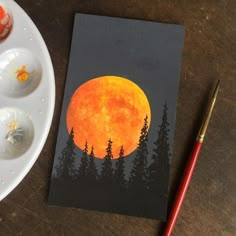 an orange full moon painted on a piece of paper next to some paintbrushes