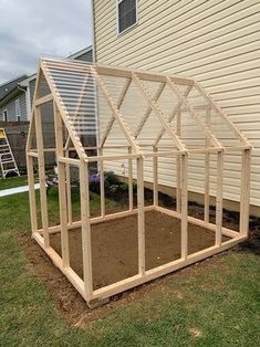 a small greenhouse built into the ground in front of a house with a ladder up to it