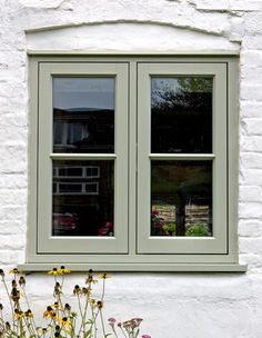 a window with two panes and some flowers in front of it on the side of a white brick building