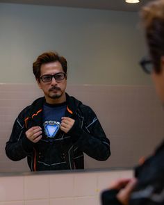 a man is looking at his reflection in the mirror while he puts on his jacket