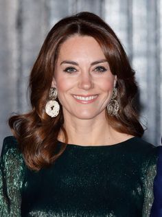 a smiling woman in a green dress with large earrings on her left shoulder and right arm