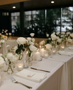 the table is set with white flowers and candles for an elegant wedding reception in front of large windows