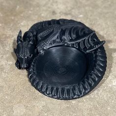 a black dragon figurine sitting on top of a cement floor next to a bowl