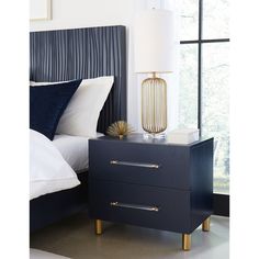 a night stand with two drawers and a lamp on it in front of a bed