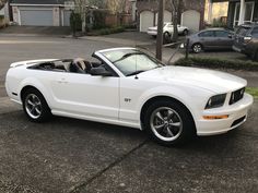 a white mustang convertible parked in front of a house