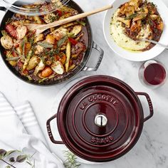 two pans with different types of food in them on a table next to wine glasses and utensils