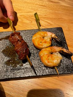 a person is holding tongs over some food on a black plate with shrimp and steak