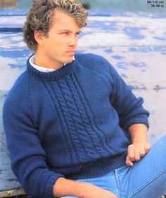 a man sitting on top of a wooden bench wearing a blue sweater and denim jeans