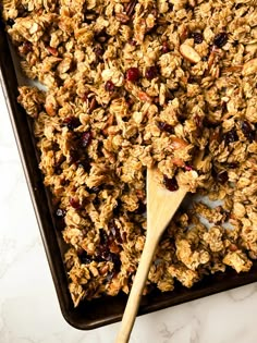 granola in a baking pan with a wooden spoon on the side and white marble counter top