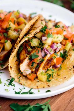 two fish tacos with pineapple salsa on a white plate and garnished with cilantro