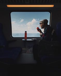 a man sitting on a train next to a window with the ocean in the background