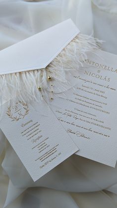 the wedding stationery is laid out on top of the bed sheet, with feathers and beads