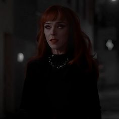 a woman with red hair wearing a black dress in a dimly lit room at night