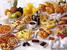 an assortment of breakfast foods on a table with fruit, bread and juice in the background