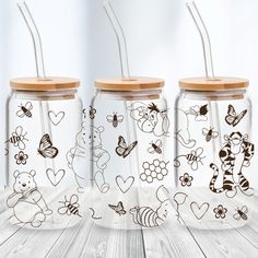 three glass jars with straws and cartoon drawings on them, sitting on a wooden table