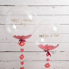 two clear balloons with pink bows and sayings on them hanging from the side of a white wooden wall