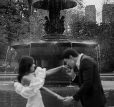 a man and woman holding hands in front of a fountain