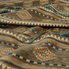 a pair of scissors laying on top of a brown and blue patterned fabric with geometric designs