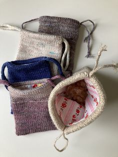 three knitted bags sitting next to each other on a white counter top, one with a teddy bear in it