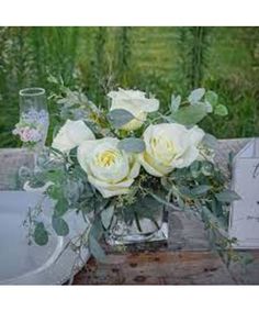 white roses and greenery in a glass vase on a wooden table with an old fashioned sink