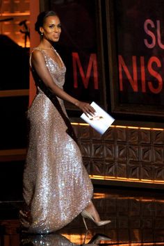 a woman in a silver dress is walking down the runway with her hand on an envelope