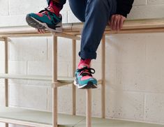 a person sitting on top of a wooden shelf next to a brick wall and wearing running shoes