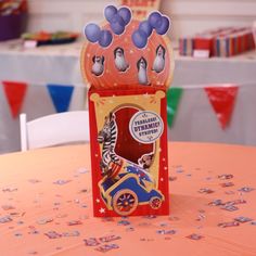 an orange table topped with a red and blue birthday card box filled with balloons in the shape of a train