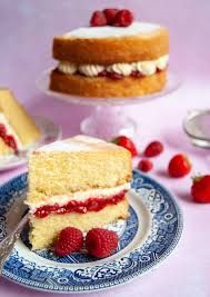 a piece of cake on a plate with raspberries next to it and another slice in the background