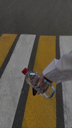 a person is holding a water bottle in their hand and crossing the street with yellow lines