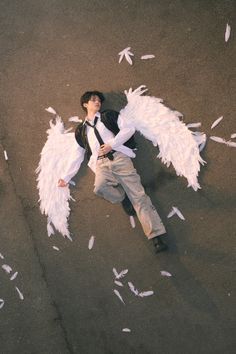 a man laying on the ground with white feathers around his body and wings in the air