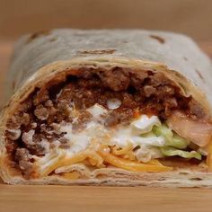 a burrito with meat, cheese and lettuce inside on a wooden surface