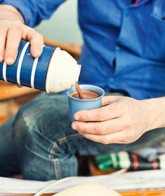 a man is sitting down and pouring something into his cup while holding a coffee mug