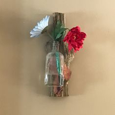 two flowers are in a glass vase on a piece of driftwood that is attached to the wall