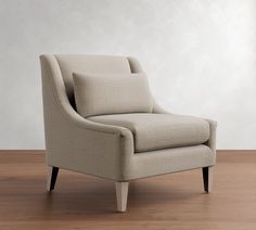 a beige chair sitting on top of a hard wood floor next to a white wall