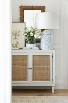 a white cabinet with wicker doors and a blue vase sitting on top of it