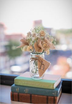 two books stacked on top of each other with flowers in a mason jar sitting on top of them