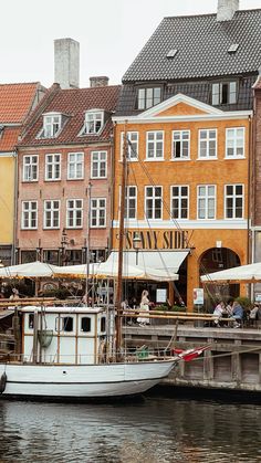 a boat is docked in the water next to some buildings and people sitting at tables