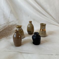 four different vases sitting on top of a white cloth covered table next to each other